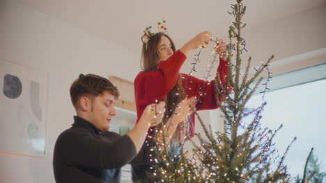 pareja decorando el árbol de navidad con luces brillantes