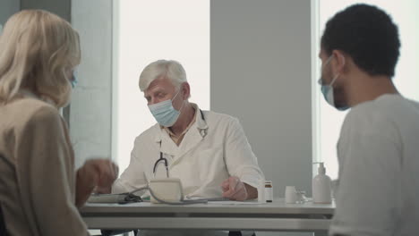 a grey haired, middle aged doctor in a facemask asking questions to a young black man