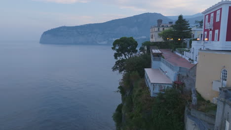 Luftaufnahmen-Von-Häusern-Und-Bäumen-Auf-Der-Klippe-In-Der-Stadt-Sorrent,-Italien,-Die-Den-Blick-Auf-Eine-Dahinter-Liegende-Wasserbucht-Freigeben