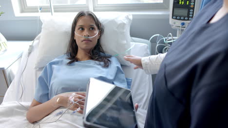 diverse female patient in hospital bed and female doctor using tablet talking, slow motion