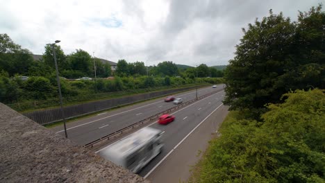 motion blurred cars going by fast timelapse on m4 motoroway with dual carriageway with trees and street lamps. busy road with multiple vehicles.