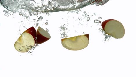segmentos de manzana sumergiéndose en el agua sobre un fondo blanco