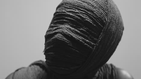 a mummy of a woman on a white backdrop rises her head