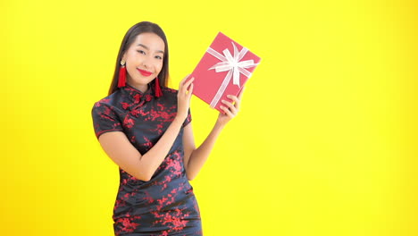 Una-Mujer-Joven-Con-Un-Vestido-Rojo-Y-Negro-De-Seda-Sostiene-Un-Regalo-Envuelto