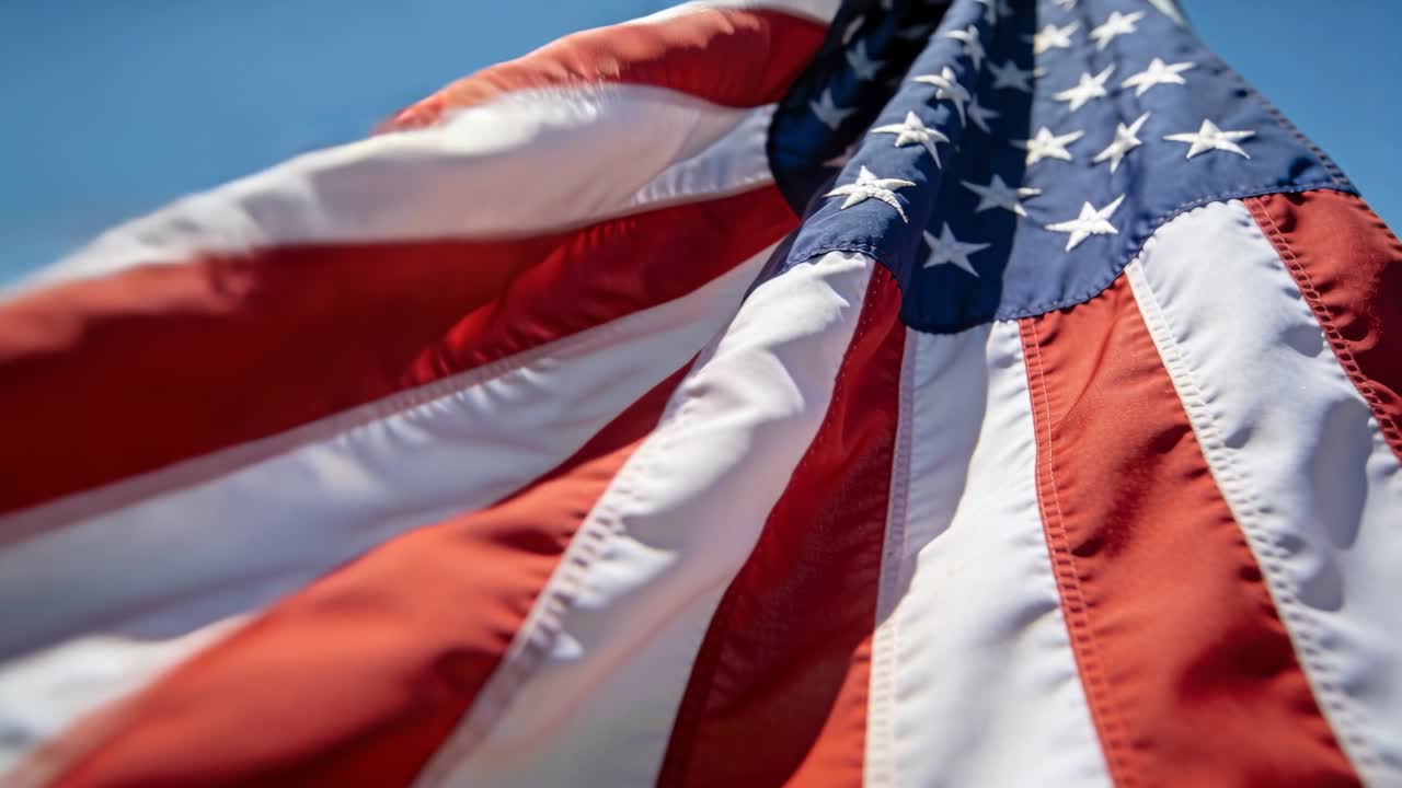 Bandiera americana sventolante che mostra cuciture e stelle contro il cielo blu, con il vento che muove il tessuto.