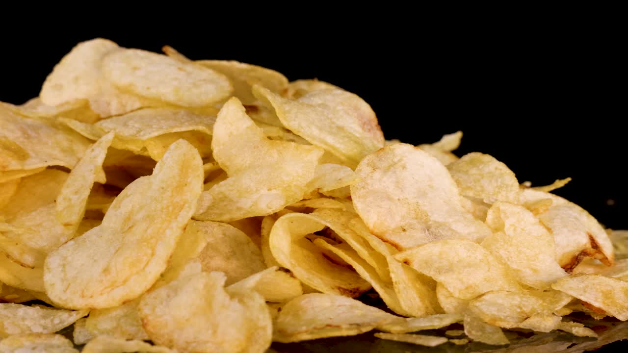 Golden potato chips rotate and zoom out, crisp texture highlighted by dramatic studio lighting