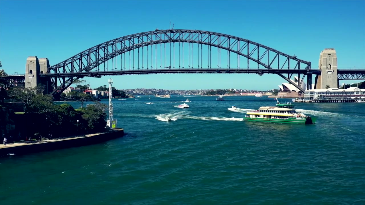 Drone che sorvola il porto di Sydney di fronte al Sydney Harbour Bridge con la Sydney Opera House sullo sfondo mentre un traghetto passa