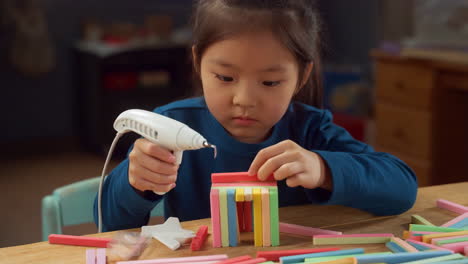 a young girl concentrated on building a structure using colorful blocks and a hot glue gun