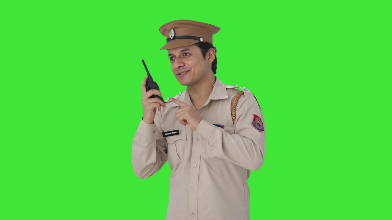 Agente di polizia indiano felice che impartisce istruzioni tramite walkie talkie su schermo verde.