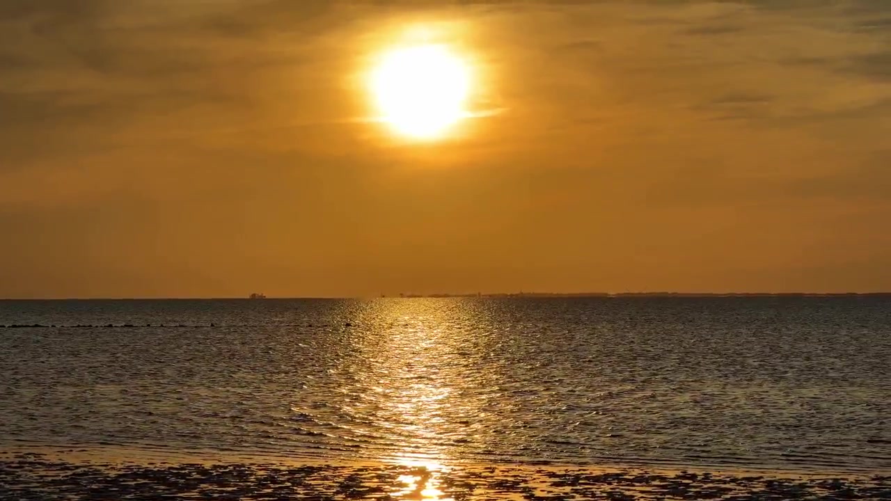 Klar solnedgang over det rolige hav, der kaster en strålende gylden refleksion på vandet.
