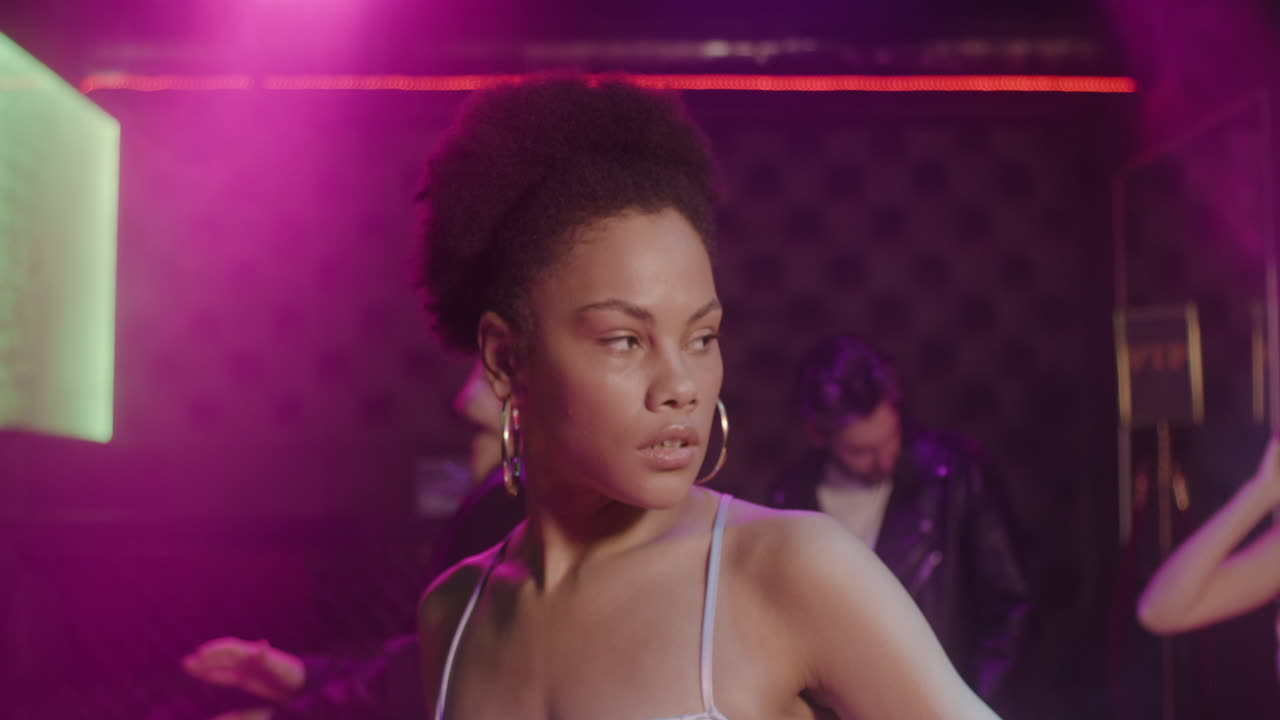 retrato de una chica hermosa que mira con confianza a la cámara en la discoteca mientras sus amigos bailan detrás de ella 1