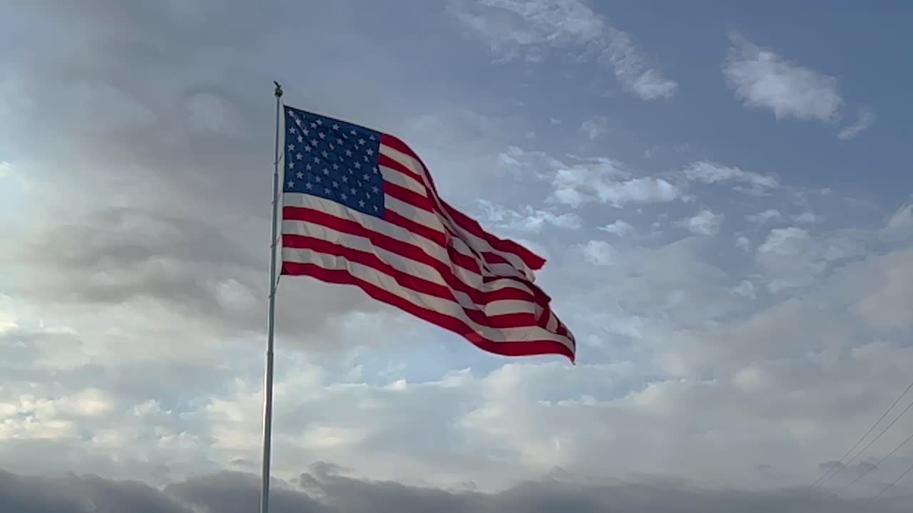 gran bandera americana súper cámara lenta soplando en el viento contra un cielo azul soleado y nubes blancas a finales de la tarde