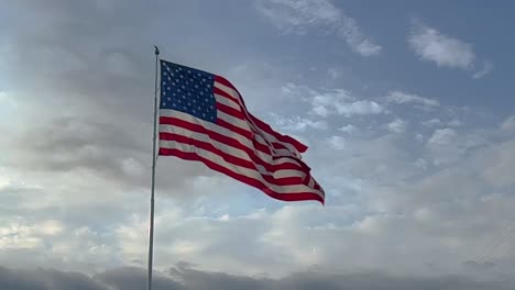 Large-American-Flag-super-slow-motion-Blowing-in-the-Wind-against-a-sunny-blue-sky-and-white-clouds-in-late-afternoon