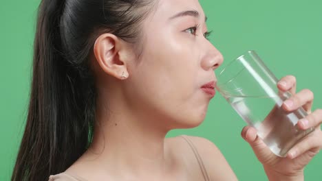 스튜디오에서 녹색 화면 배경에 서서 카메라를 향해 미소 짓는 아시아 여성의 근접 측면 시각
