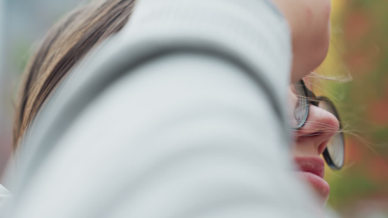 Close up of young woman wearing glasses with her hair swaying in wind while man hand gently adjusts her hair, capturing soft intimate moment between couple outdoors during breezy day