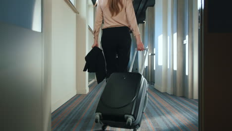 businesswoman with travel suitcase walking at hotel corridor