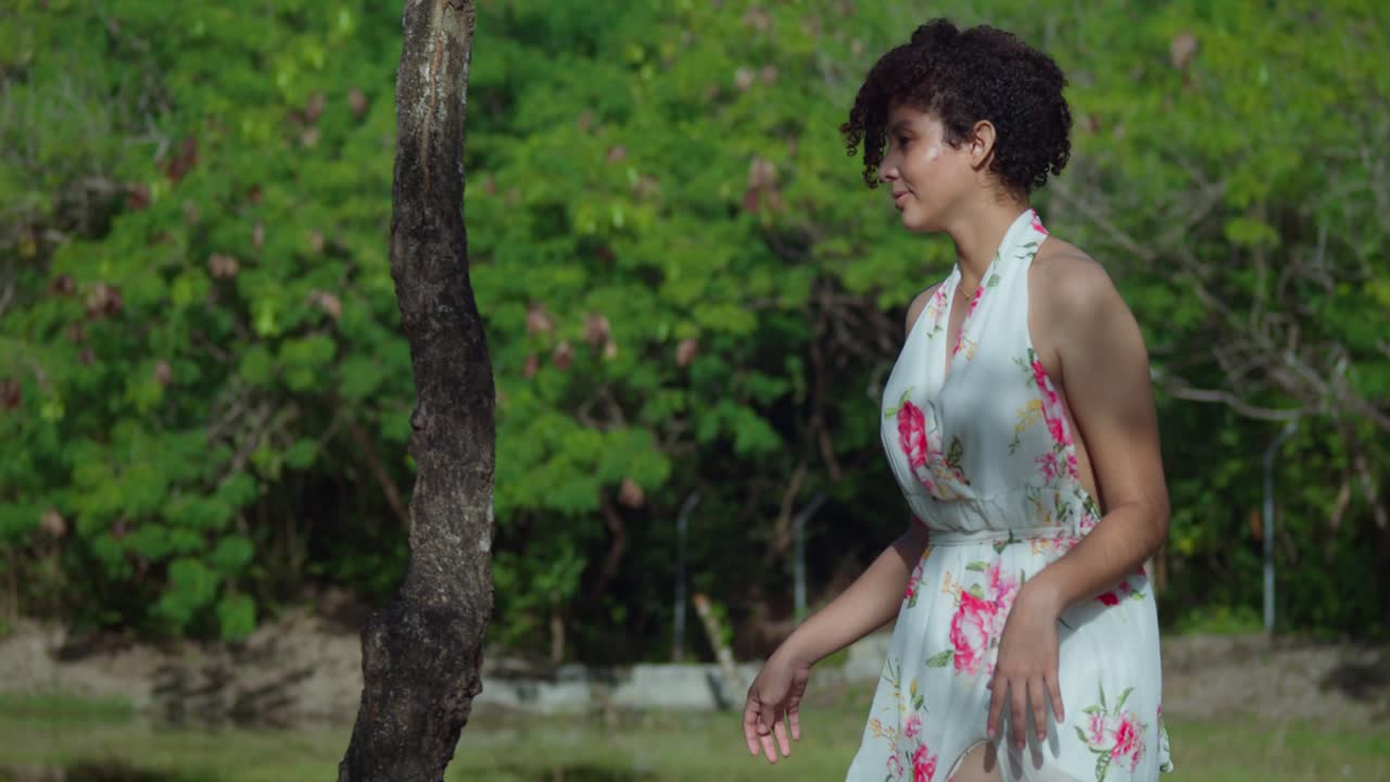 꽃무늬 드레스를 입은 어린 소녀가 공원에서 화창한 날 나무 줄기를 들고 걷고 있다