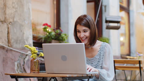 Glückliche-Touristin-Nutzt-Laptop-Computer-Und-Feiert-Den-Sieg-Mit-Guten-Botschaftsnachrichten-Auf-Der-Terrasse-Eines-Städtischen-Stadtcafés