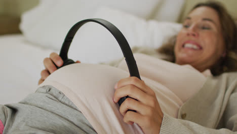 midsection of happy caucasian pregnant woman holding headphones over belly