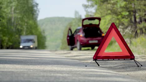 emergency stop sign on a forest highway in front of a broken car.