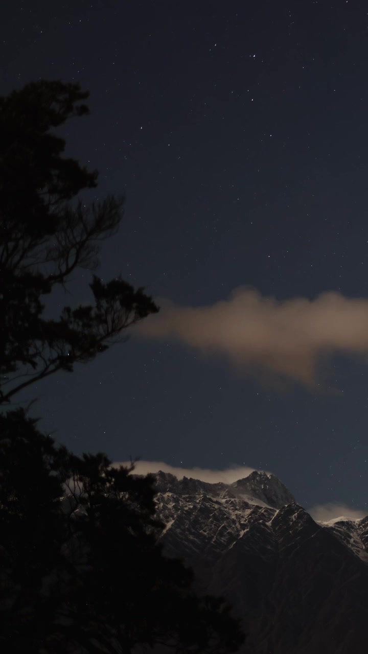 Un cielo notturno sereno con stelle e nuvole sopra montagne innevate, catturato a Queenstown, Nuova Zelanda.