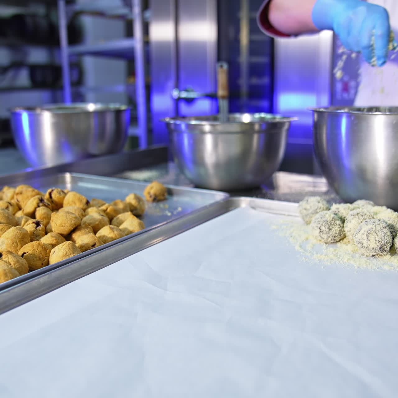 Cookies being coated with sprinkling. Worker shaking metal bowl in hands to cover all sweets with coconut flakes