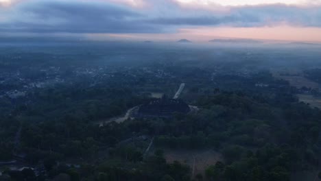 Luftaufnahme-Eines-Nebligen-Morgens-Auf-Dem-Komplex-Des-Borobudur-Tempels,-Wenn-Es-Vor-Sonnenaufgang-Noch-Dunkel-Ist-Und-Ein-Orangefarbener-Himmel-Herrscht