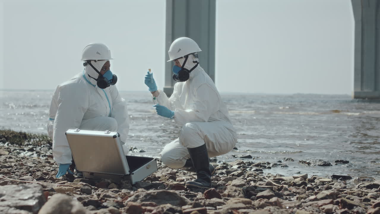 Two Ecologists in Coveralls Discussing Samples of Polluted Water