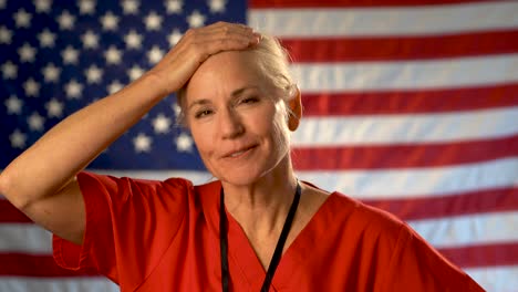 medium tight portrait of nurse looking at the camera, relieved and very happy with a us flag behind her