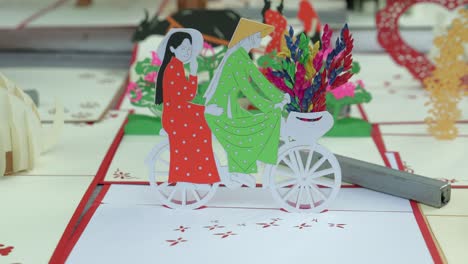 a stationary footage of a cycling couple paper craft with added flowers design on their bicycle's basket. this was shot in hội an, a city in vietnam.