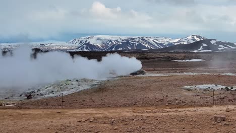 a breathtaking shot captures the sulfuric smoker landscape near myvatn at reykjahlid in iceland, with billowing smoke and a majestic mountain range in the background