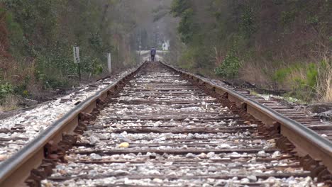 an old black man walks in the distance on lonely railroad tracks