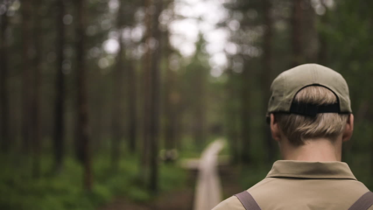 Inquadratura ravvicinata che segue un giovane uomo con un cappellino che cammina attraverso una foresta verde.