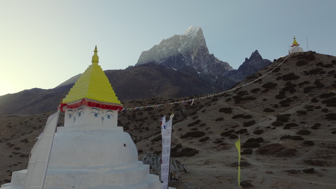 Panoramatický letecký záběr dronu oddalující se od bílé buddhistické stúpy s modlitebními vlajkami v Dingboche, Nepál, odhalující okolní himálajské hory podél trasy treku do základního tábora Everestu