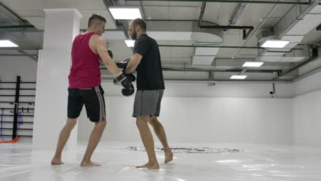 en el entrenamiento en las peleas mixtas el hombre golpea una rodilla en las patas del entrenador en un salto. movimiento lento.