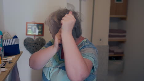 older fat woman brushing her hair with a comb, styling and creating volume in front of mirror inside the bathroom