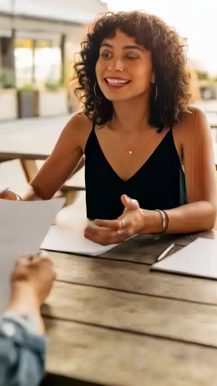 Video verticale: Riceve un foglio, una donna con un top nero legge appunti per una riunione su un patio con un tablet.