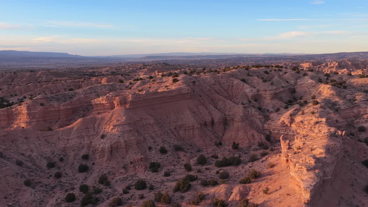 Wide aerial view captures the deep ridges and eroded sedimentary layers of high desert badlands. The arid landscape features textured sandstone formations and sparse brush in northern New Mexico