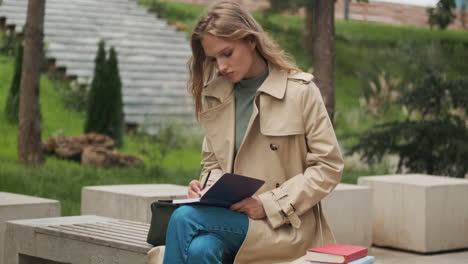 caucasian female student writing in notebook at the park.