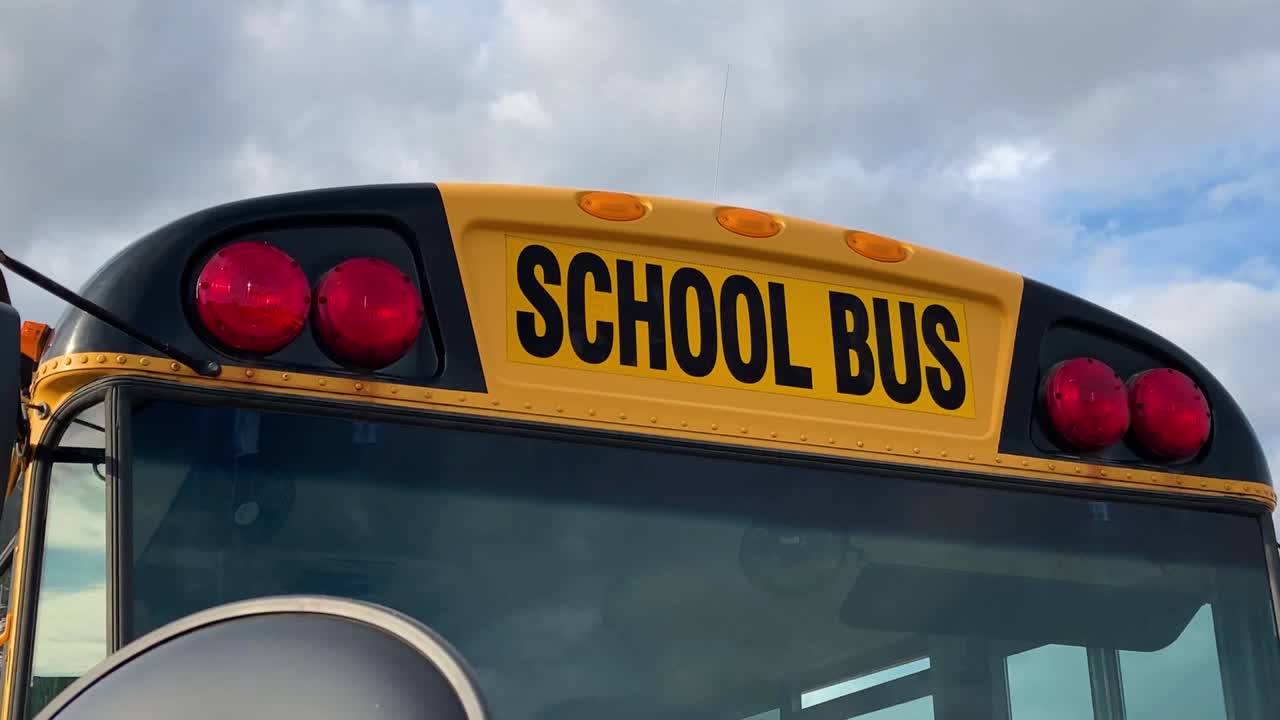 Skolebus nærbillede, venstre side, viser røde lygter og spejle mens den holder parkeret; beskåret