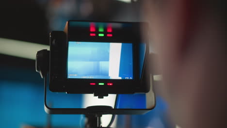camera monitor displaying broadcast studio setup with red, green lights indicating status. camera in focus, background blurred with blue lighting, indicating tv production or broadcast environment