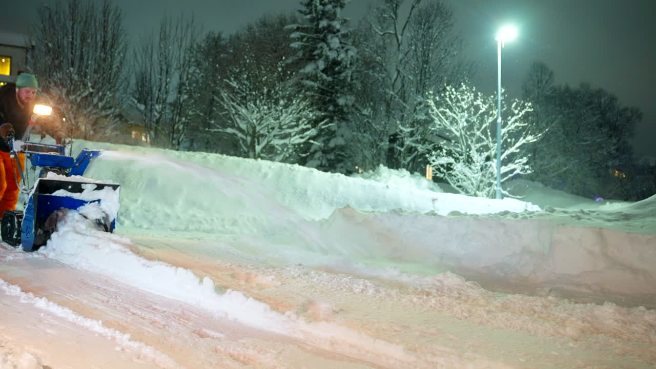 An adult man using snowblower gasoline machine to clear deep snow after heavy snowfall at night