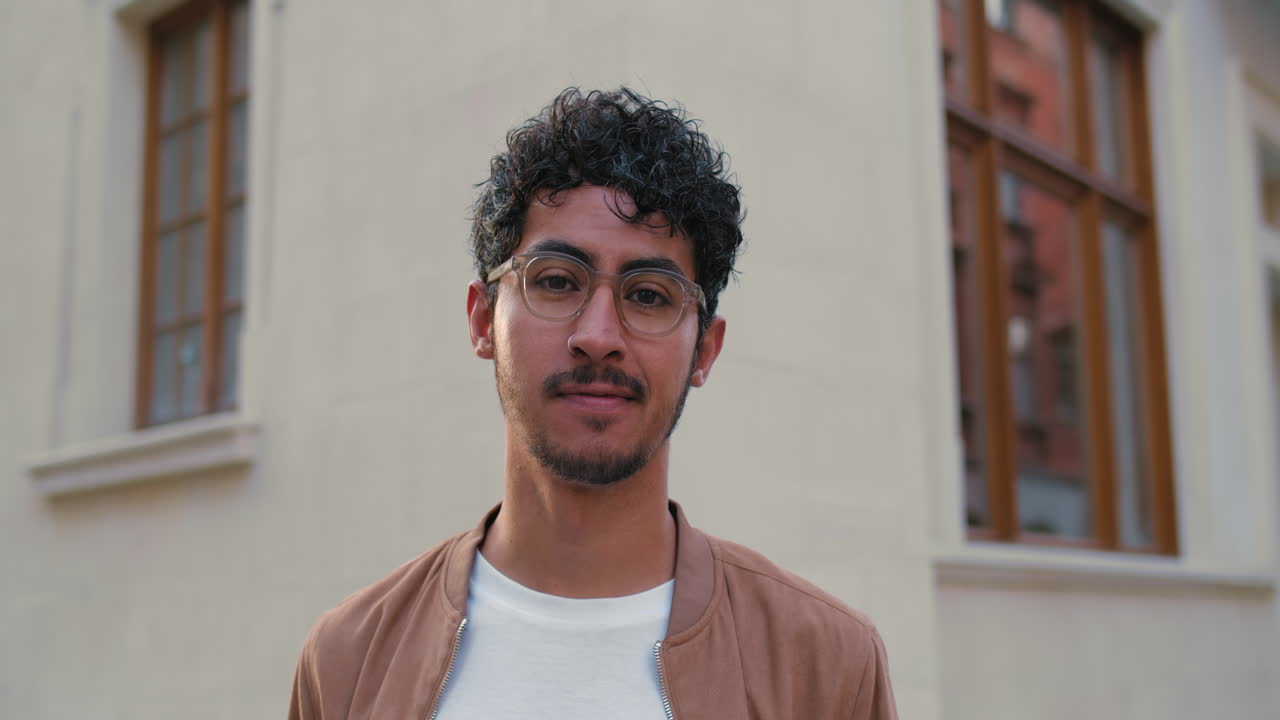 Portrait of a man with curly hair and glasses in front of a building