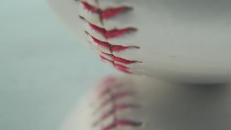toma macro cinematográfica de una pelota de base blanca, primer plano en puntos rojos, béisbol en un espejo que refleja un soporte brillante, luz de estudio profesional, video 4k inclinado hacia arriba