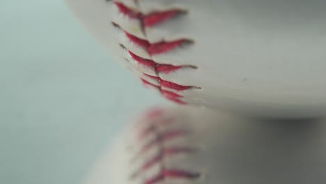 cinematic macro shot of a white base ball, close-up on red stitches, baseball on a mirror reflecting shiny stand, professional studio light, 4k video tilt up