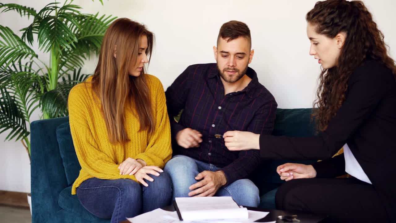 la mujer de negocios está vendiendo la casa a una pareja casada, el marido feliz está firmando el acuerdo de compra y venta, estrechando la mano al agente de bienes raíces y tomando la llave y luego besando a su esposa.