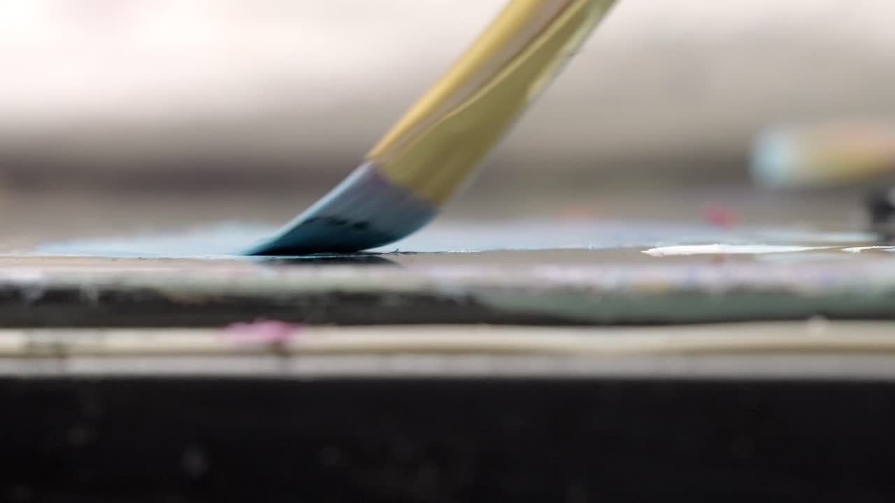 Close-up extremo de um pincel misturando tinta azul na paleta de um artista