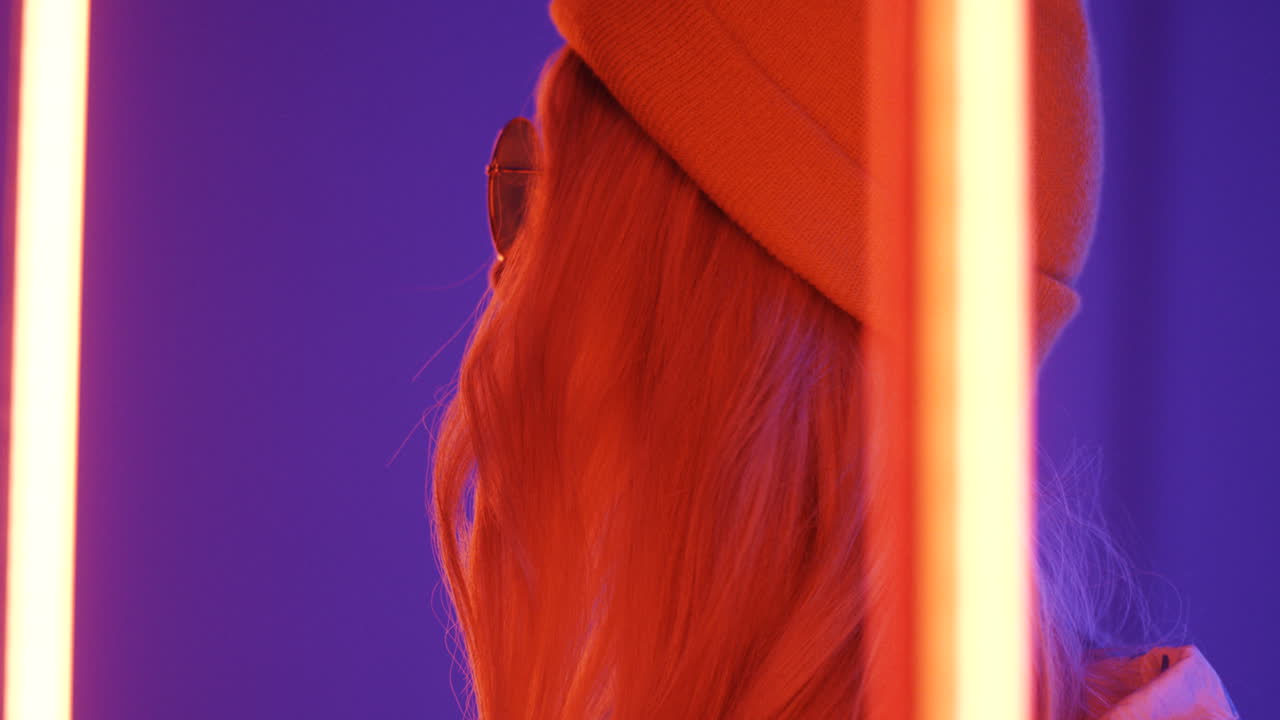 cerca de una joven rubia hermosa mujer con sombrero y gafas sonriendo a la cámara con luces de neón