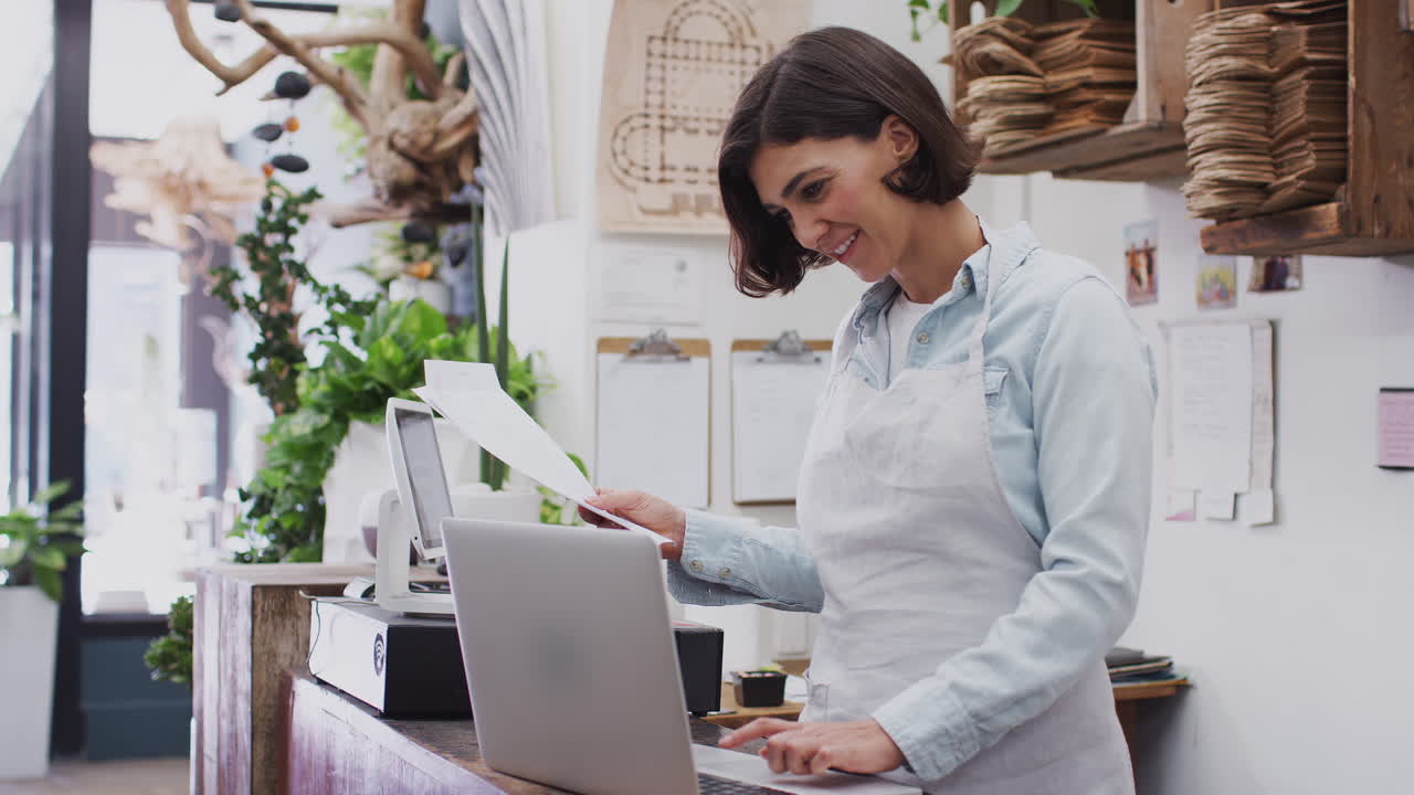 Assistente alle vendite femminile che lavora al computer portatile dietro il banco di vendita del negozio di fioristi