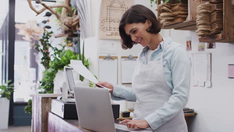 asistente de ventas femenina trabajando en una computadora portátil detrás del escritorio de ventas de una tienda de flores